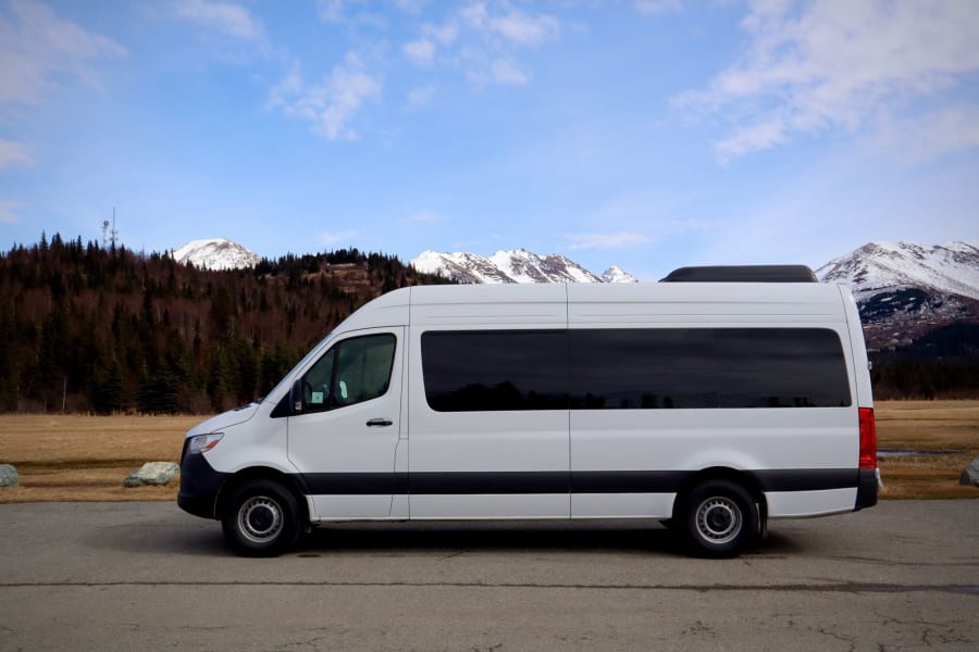 White RV rental van parked on an asphalt lot, showcasing snowy mountains and a blue sky backdrop.