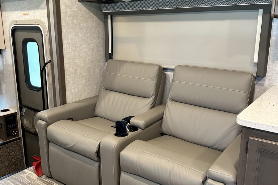 Relax in this RV rental! View of modern interior with twin recliners, overhead cabinets, window, and entry door.