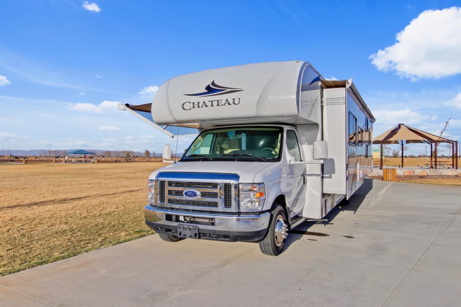White Class C Chateau RV rental with awning extended, parked on concrete outdoors under a blue sky.