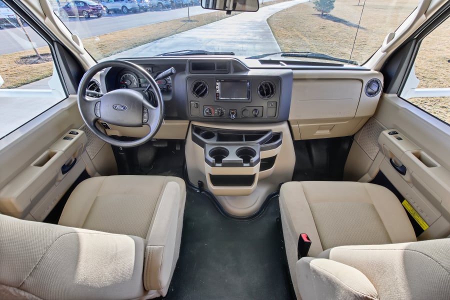 Overhead view of an RV rental's Ford E-Series cockpit, showing dash, steering wheel, and light beige seats.