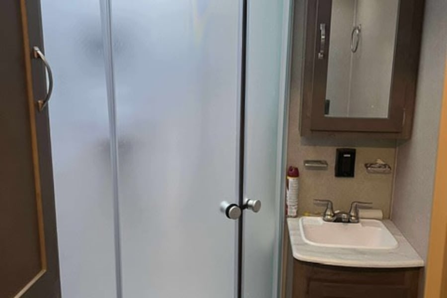 Inside an RV rental bathroom: compact design with frosted glass shower, sink, and mirrored medicine cabinet. Functional space.