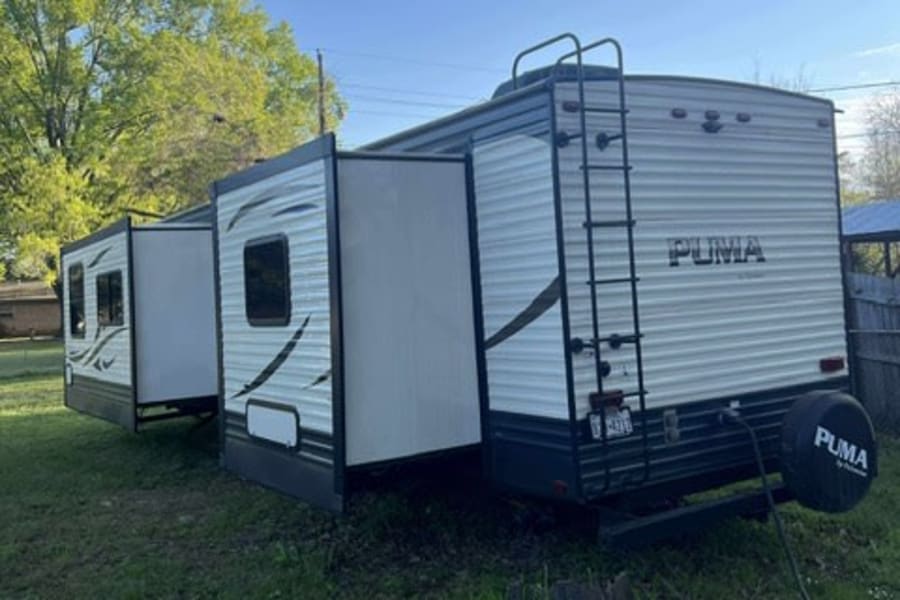 This Puma travel trailer, a ready-to-go RV rental, is shown with its slide-outs extended in a grassy outdoor setting.