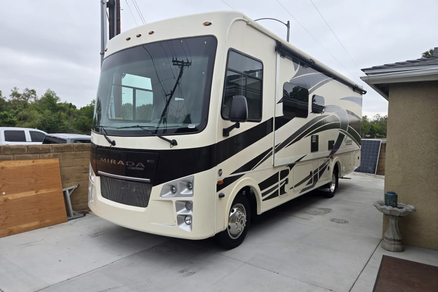 Large, cream-colored Coachmen Mirada RV parked on a driveway, ready for adventure. Perfect for your next RV rental trip.