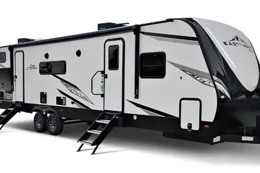 White and black East To West Alta travel trailer, with slide-out and steps deployed, ready for RV rental.