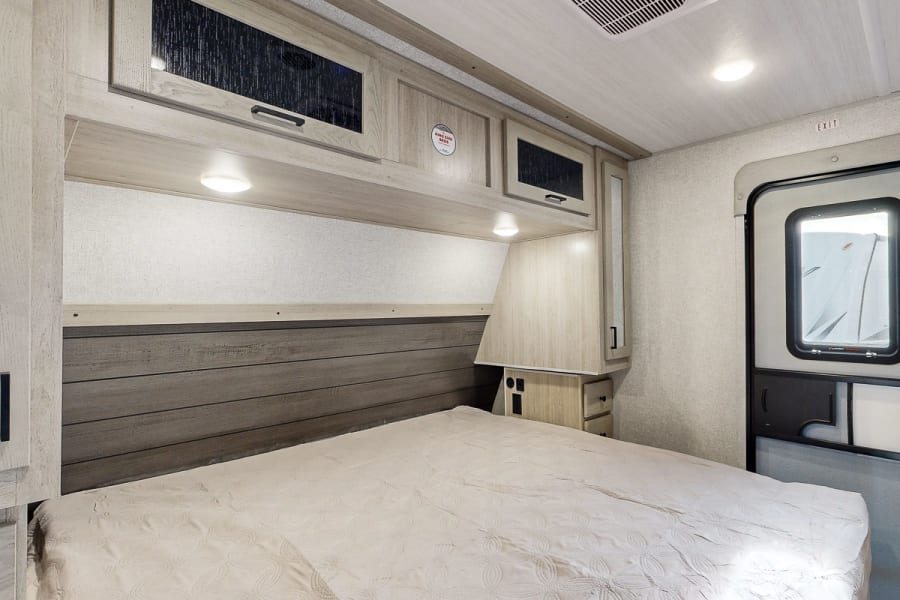 Inside a spacious RV rental bedroom, showcasing a queen bed, wood paneling, and convenient overhead cabinets.