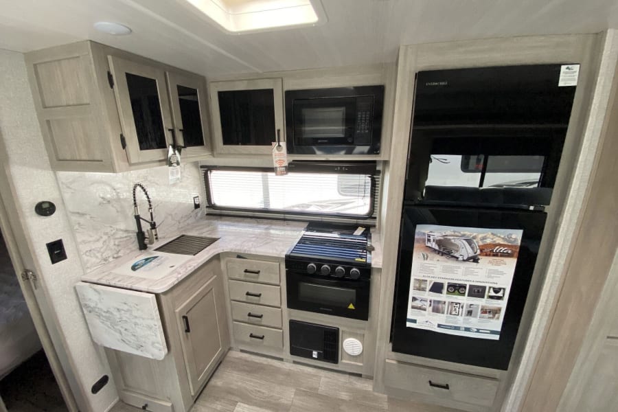 RV rental kitchen featuring light wood cabinets, marble-look counters, sink, microwave, stove, and full-size fridge.