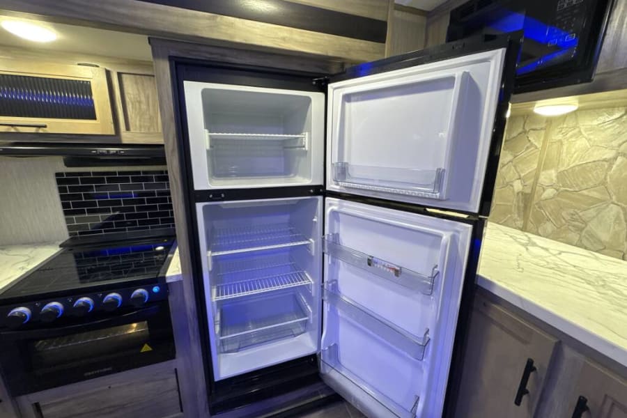 Explore this RV rental's kitchen: open fridge, black stove/oven, black subway tile, and overhead microwave. Ready for trips!