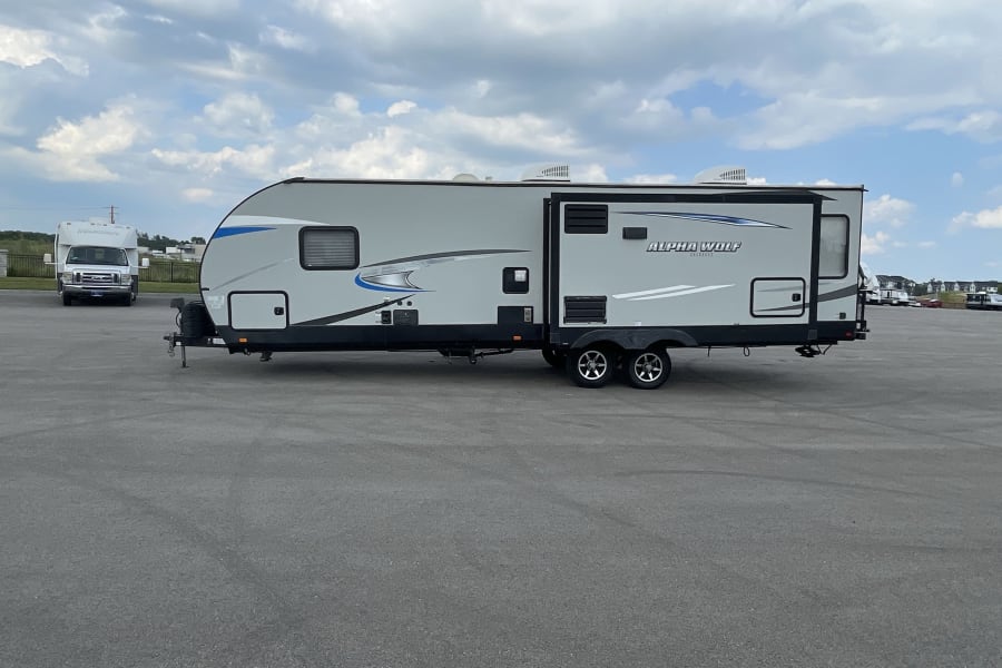 Alpha Wolf travel trailer RV rental, parked on a large asphalt lot. Ready for adventure under a cloudy sky.