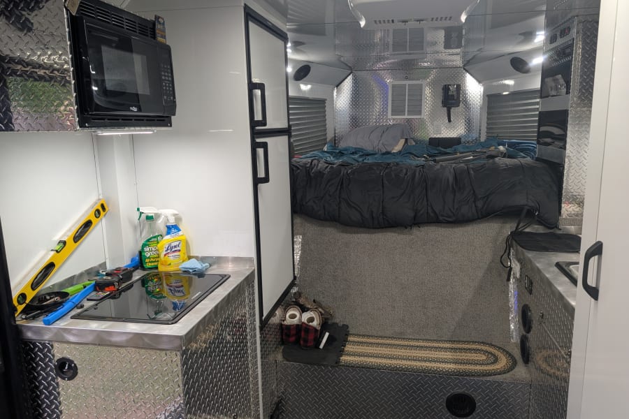 Modern rv rental interior with a compact kitchen, bed area, microwave, fridge, and rugged diamond plate details.