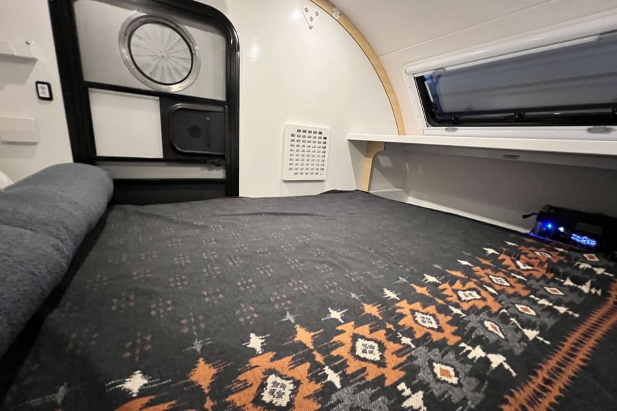 Cozy RV rental interior: a comfortable bed, entrance door, wall vent, and side window for compact travel.