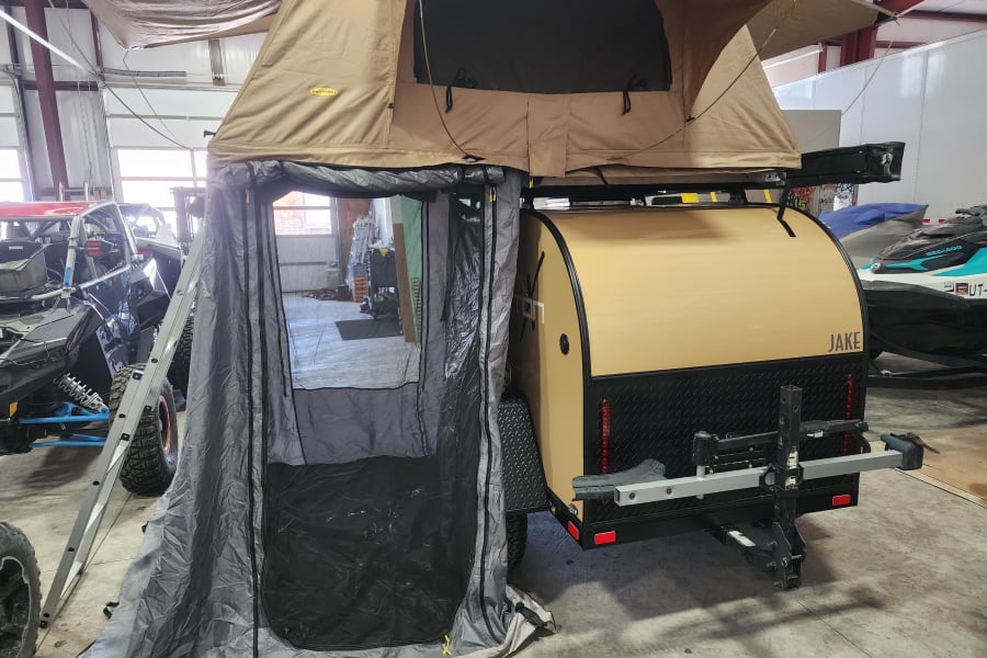 Teardrop trailer with rooftop tent and annex setup, ideal for rv rental adventures. UTV & jet ski also shown in garage.