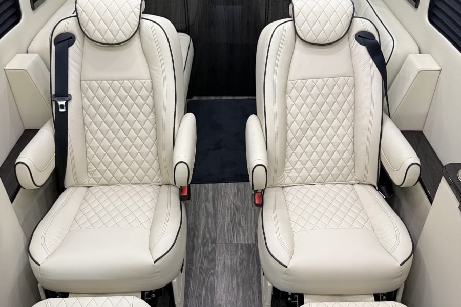 Experience luxury: RV rental interior with two plush cream quilted leather seats, wood paneling, and an entertainment screen.