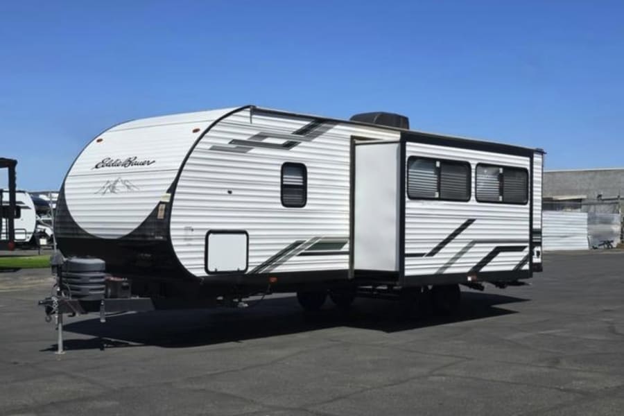 A white Eddie Bauer travel trailer RV rental with black and green accents, parked under a blue sky, ready for adventure.