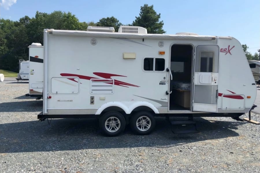White travel trailer RV rental with red graphics, door open, parked on gravel, ready for adventure.