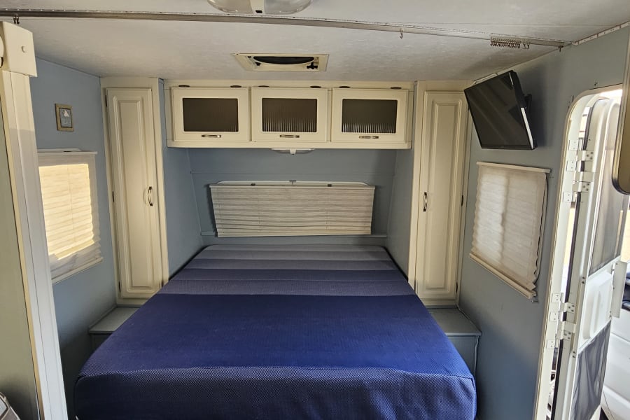 Cozy RV rental interior with a spacious bed, light blue walls, and a classic checkerboard floor, offering compact comfort.
