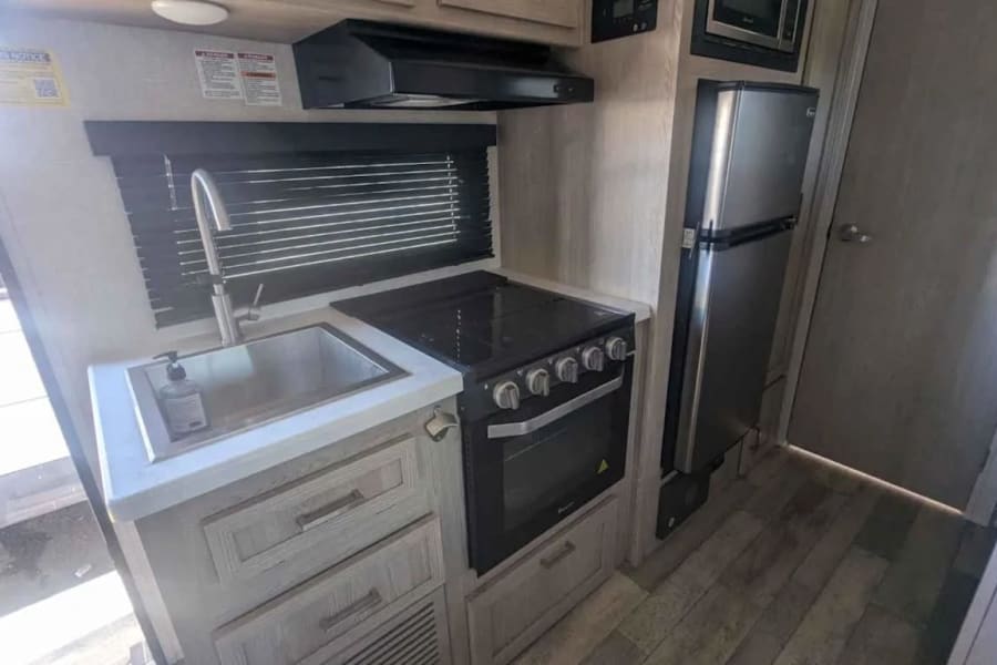 Modern RV rental kitchen featuring a compact design with a stainless steel sink, stove, oven, and refrigerator.
