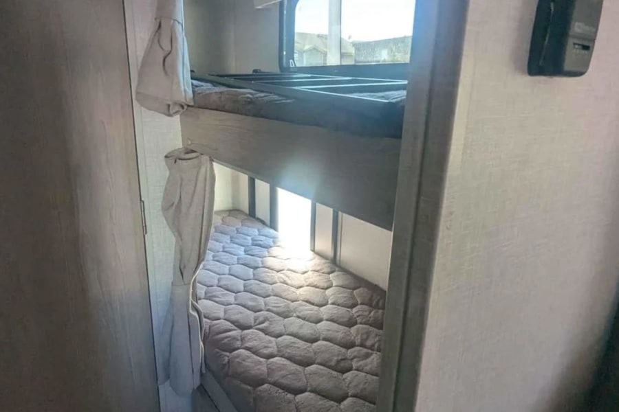 Inside an RV rental: view of comfortable bunk beds with soft mattresses, privacy curtains, and a ladder for the top bunk.
