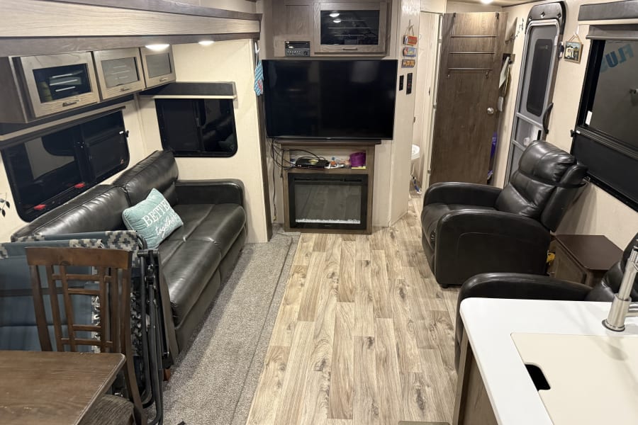 Spacious RV rental interior featuring a cozy living room with leather furniture, TV, fireplace, and dining area.