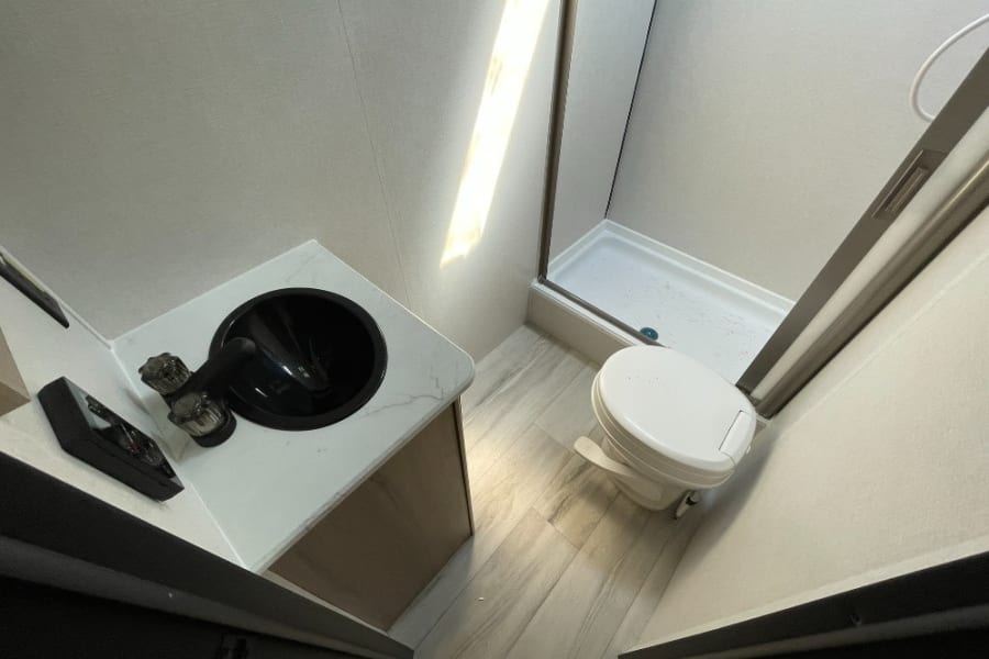 RV rental bathroom: modern vanity with black sink, white toilet, and glass-enclosed shower.