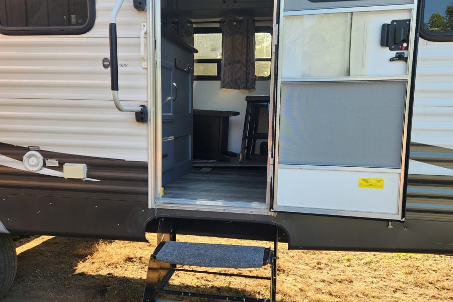 Open RV rental door with grey carpeted steps leading to a functional interior, ready for your next adventure.