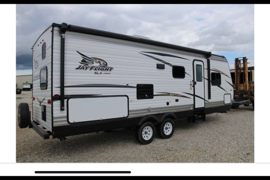 White Jayco Jay Flight SLX recreational vehicle (RV rental), a travel trailer with an awning, spare tire, and dual axles.