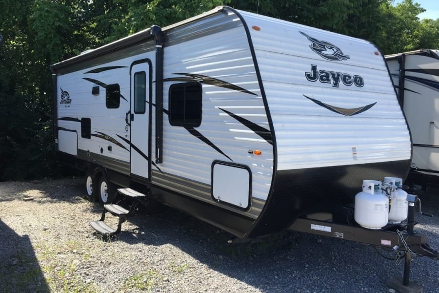 White Jayco travel trailer with awning and propane tanks, parked on gravel. Perfect for RV rental adventures.