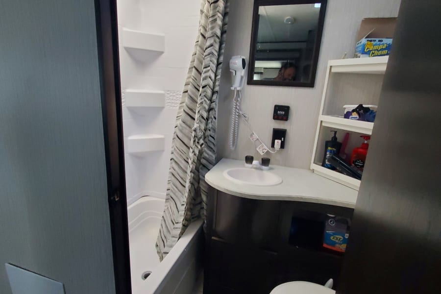 Inside an rv rental: a compact bathroom with shower, sink, toilet, and mirrored vanity.