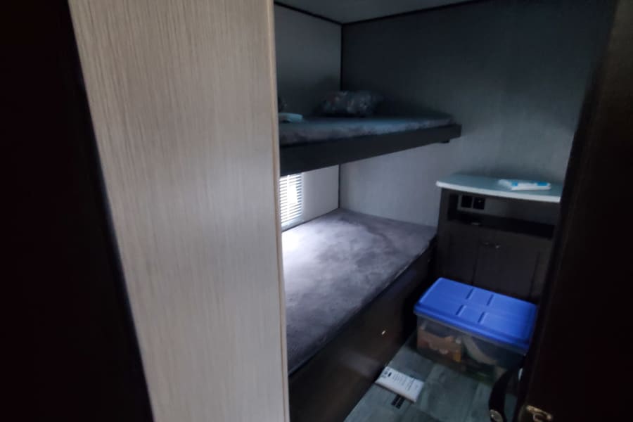 This RV rental offers a practical interior with cozy bunk beds, a window, and a storage cabinet, ideal for a compact space.
