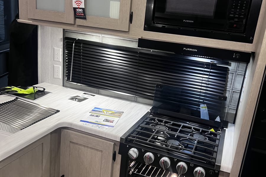 Modern RV rental kitchen with open oven, gas range, Furrion microwave, wood cabinets, and sink. Ready for your next trip!