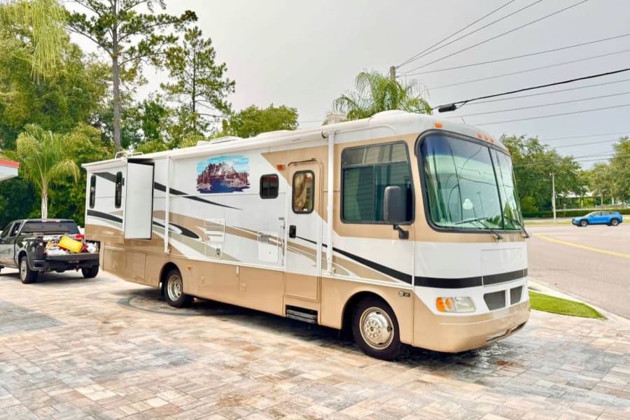 A spacious white and tan motorhome RV rental, with an extended slide-out, is hitched to a truck and parked on pavers.