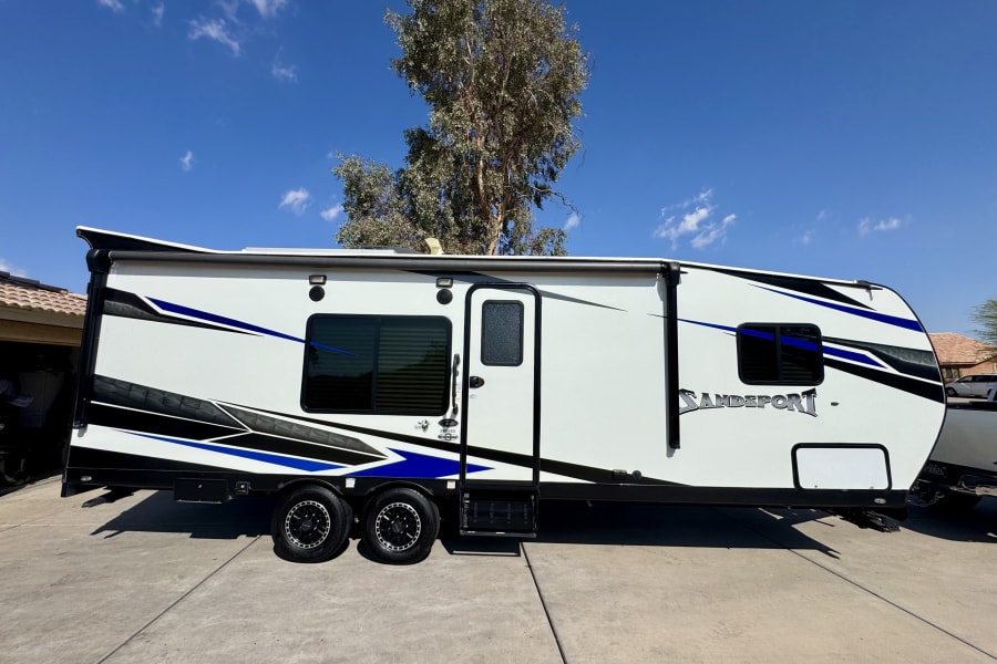 Modern white SandSport toy hauler RV rental with bold black & blue graphics, ready for travel and camping adventures.