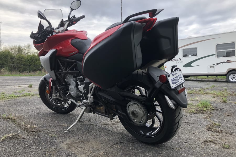 Red motorcycle with panniers parked on asphalt, an RV rental visible behind it. Perfect for adventure travel.