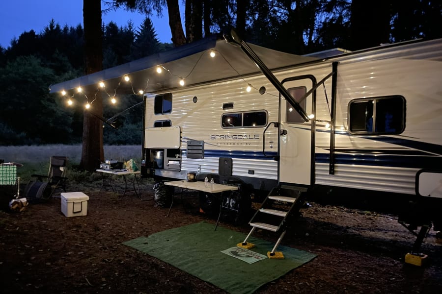 Nighttime rv rental camping: A cozy recreational vehicle adorned with string lights under its awning, set in a dark forest campsite.