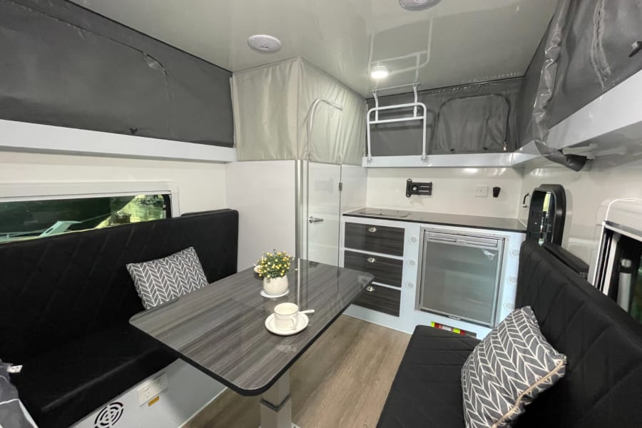Modern RV rental interior with dining benches, kitchen, and bunk beds overhead. Ideal for family adventures.