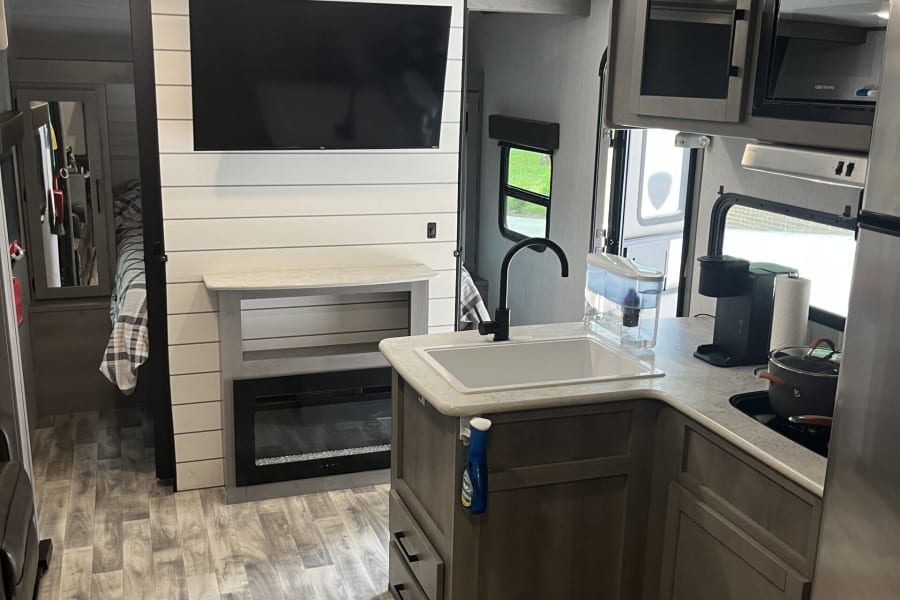 Modern RV rental interior featuring a well-equipped kitchen, inviting living area with TV and fireplace, and a cozy bedroom.