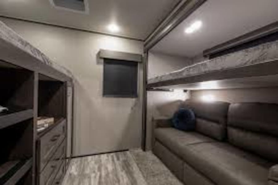 RV rental bunkhouse interior: multi-level bunks, sofa, & dresser for cozy family travel. Brightly lit cabin space.