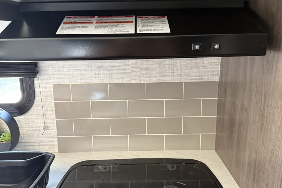 Compact RV kitchen with a two-burner gas cooktop, range hood, and tiled backsplash, perfect for an rv rental.