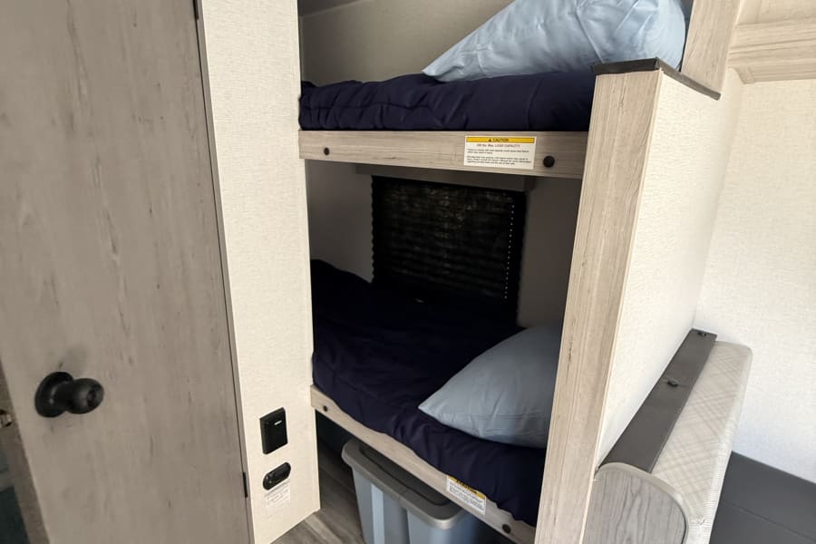 Comfortable bunk beds within an rv rental, featuring navy mattresses, light wood frames, storage, & dinette area.