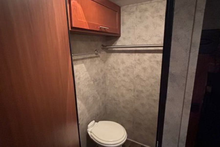 Step into this RV rental's compact bathroom, featuring a toilet, overhead cabinet, vent, and handy hanging rod.