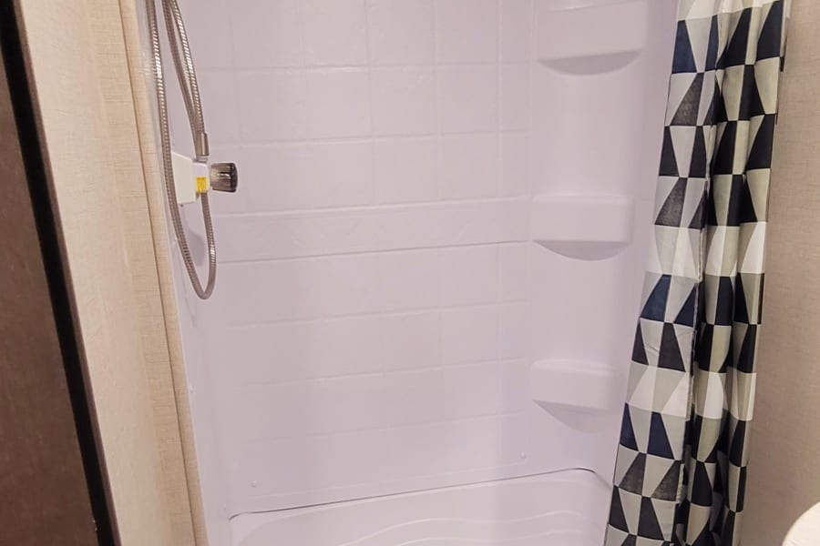 Compact RV rental bathroom features a white toilet, shower with a geometric curtain, and skylight.