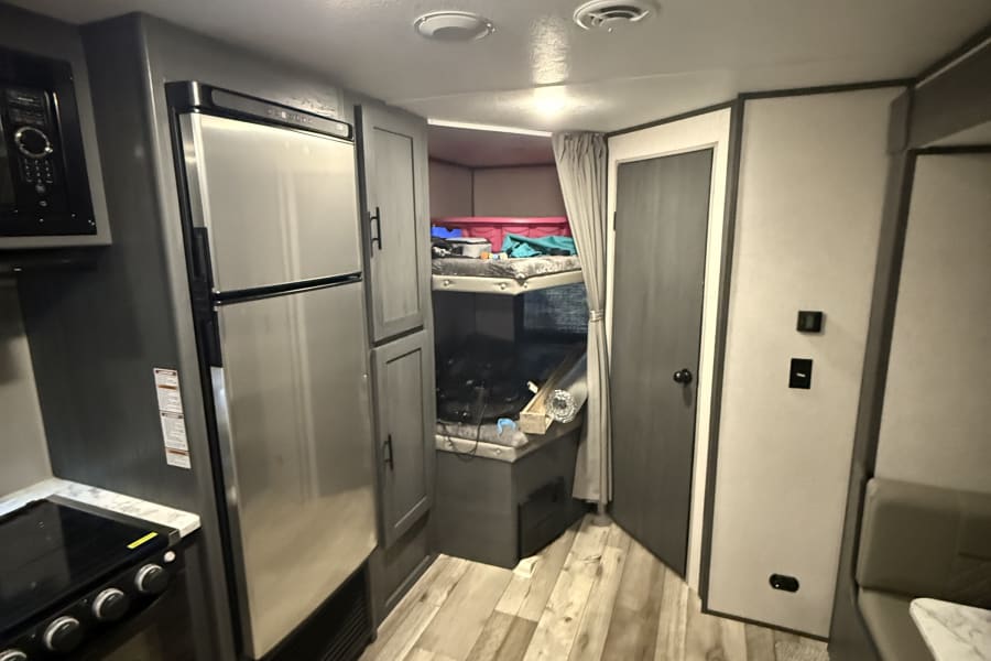 Bright RV rental interior with kitchen, bunk beds, and dinette, featuring light wood-look flooring.