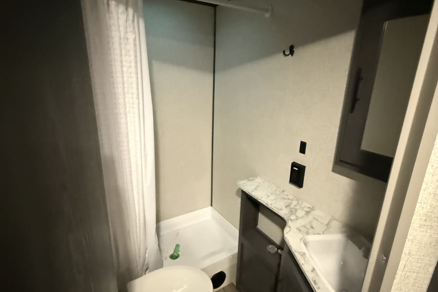 This RV rental's compact bathroom includes a shower, toilet, and vanity with a sink, optimized for travel space.