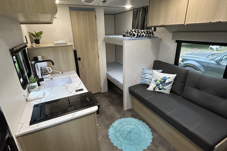 Experience a modern RV rental: well-lit interior with kitchenette, cozy sofa, and bunks, offering comfort for your camper journey.