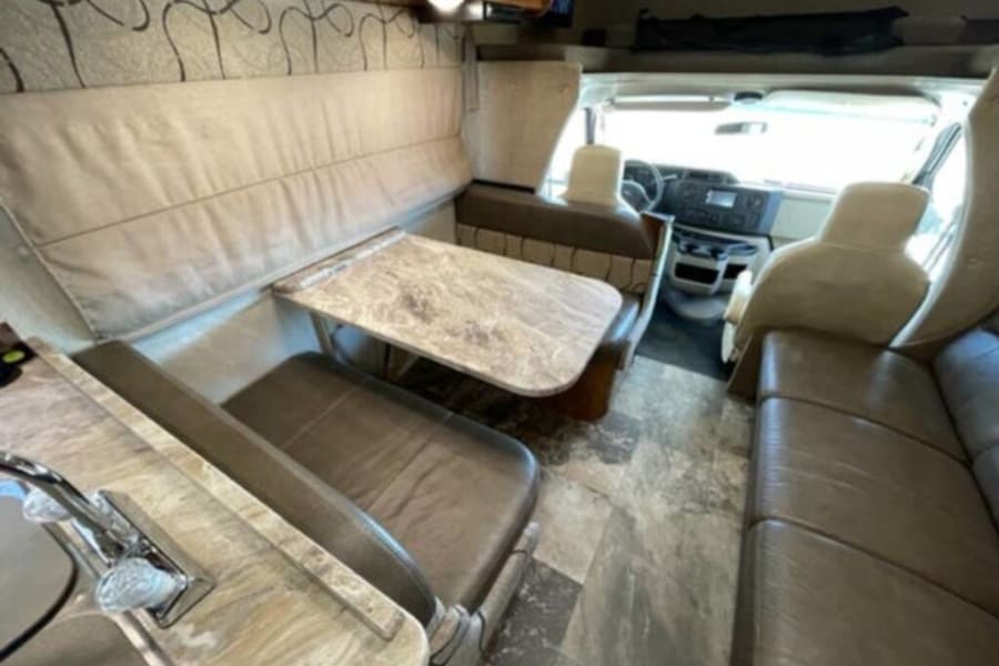 Step inside this RV rental, showcasing a comfortable dinette, functional kitchen, and bright cockpit area.