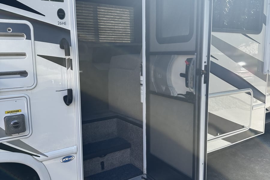 Open door of a white & grey RV rental reveals steps leading to the interior. Exterior shows 'Freedom Elite' branding and 'Camping World' decal.