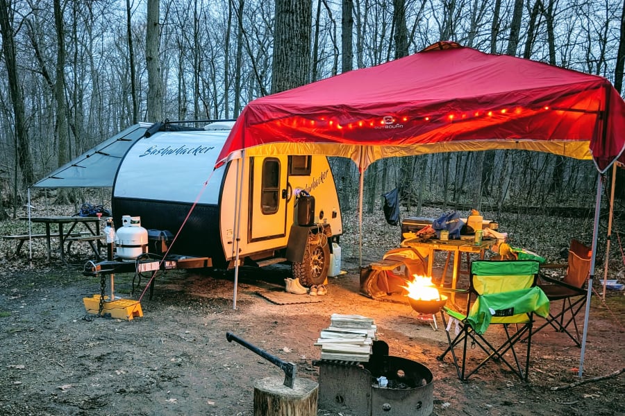 Enjoying a cozy campsite. This Bushwhacker RV rental and Outbound canopy offer comfortable outdoor living with a warm campfire.