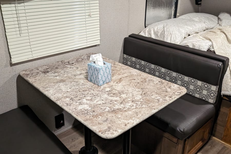 Cozy RV rental interior showing a dinette with a light table, benches, and a glimpse of the bed area.