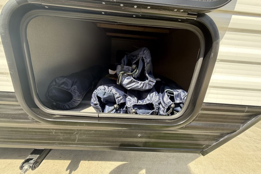 Open RV rental storage bay, revealing blue drawstring bags and various camping supplies inside.