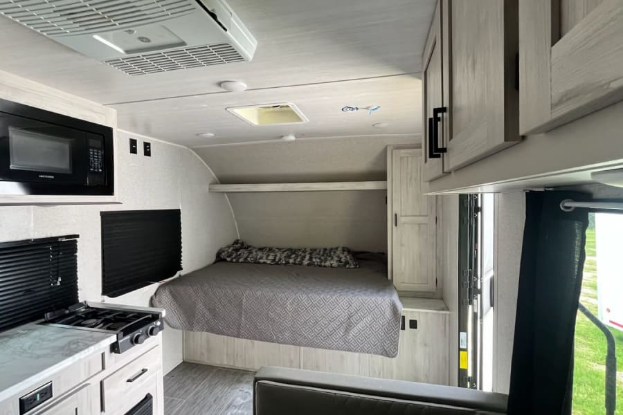 RV rental interior with compact kitchen, microwave, stove, comfy bed, and storage. Ideal for road trips.