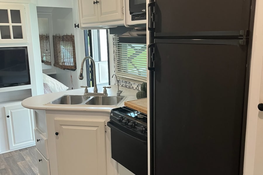 Spacious RV kitchen featuring a double sink, black refrigerator, stove, and microwave for your comfortable RV rental.
